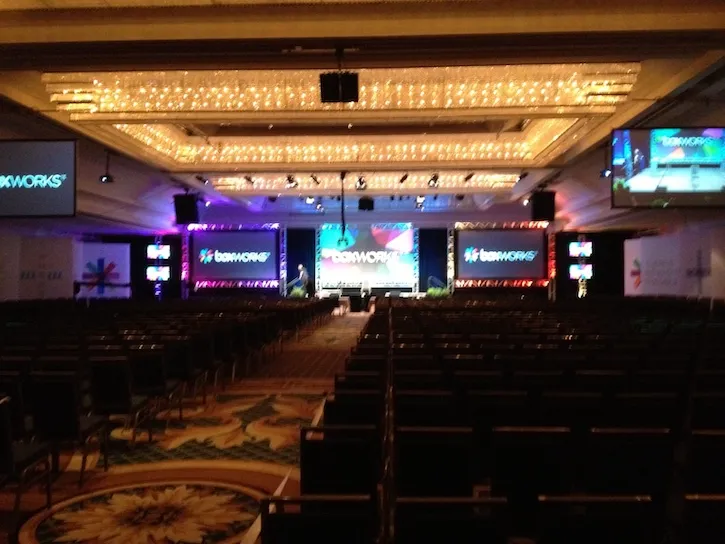 BoxWorks conference hall viewed from the back, with rows of chairs facing a brightly lit stage.